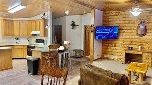 A wooden interior with a kitchen, dining area, and living room, featuring wooden cabinets, a TV, and mounted animal heads. - Wexford Hollow 6 BR Cabin with Swimming Pool & Hot Tub (Lansing)