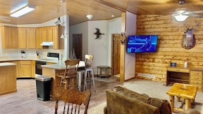 A wooden interior with a kitchen, dining area, and living room, featuring wooden cabinets, a TV, and mounted animal heads.