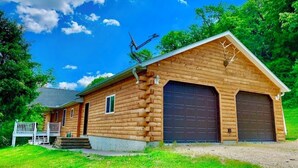 A log cabin with a front porch, two garage doors, and a satellite dish. - Wexford Hollow 6 BR Cabin with Swimming Pool & Hot Tub (Lansing)
