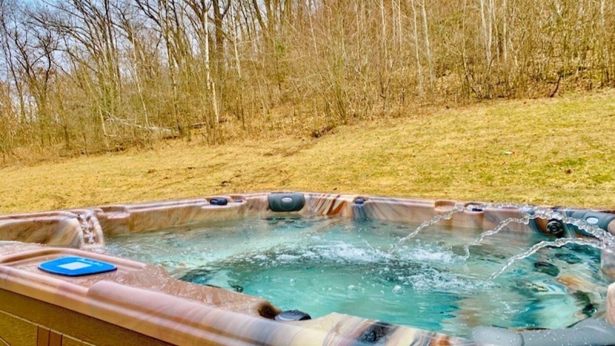 A hot tub with water jets, surrounded by a grassy area and trees.