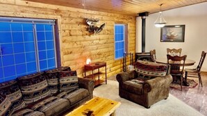 A log cabin interior with a sofa set, a dining table with chairs, and a fireplace. - Wexford Hollow 6 BR Cabin with Swimming Pool & Hot Tub (Lansing)