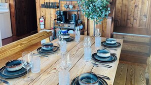 A wooden dining table set with plates, glasses, and cutlery, a coffee machine, and a clock on the wall.