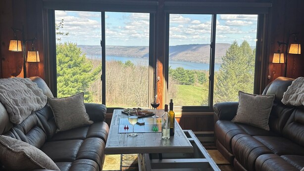A room with two leather sofas, a coffee table, and large windows offering a view of a lake and hills.