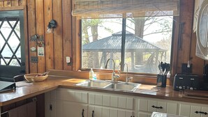 A wooden cabin-style kitchen with a large window, a sink, and a stove.