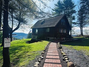 Ein Holzhaus mit einem Ziegelweg, der davor führt, umgeben von Bäumen und einer Rasenfläche.