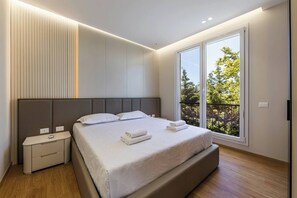 A modern bedroom with a large bed, bedside tables, and a balcony with a view of trees. - White Escape | 3BR Luxury Lalzi Beach Villa (Gjiri i Lalzit)