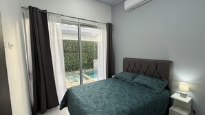 Un dormitorio con cama, mesita de noche, aire acondicionado y vistas a una piscina.