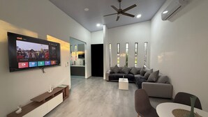 Una sala moderna con televisor de pantalla plana, ventilador de techo y comedor con mesa y sillas.