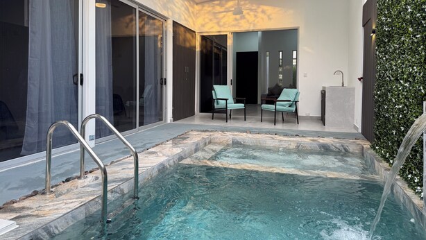 Un área de piscina interior moderna con vista despejada, un ventilador de techo y una zona de estar con sillas.