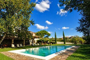 A swimming pool with a stone border, surrounded by grass and trees, with a clear sky above. - Apartment in Castelnuovo Berardenga (Castelnuovo Berardenga)