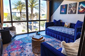A room with a large window, a blue sofa, a round coffee table, and a patterned rug. - Unbelievable Oasis with Private Pool, Spacious and Resort Home (Goodyear)