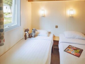 Ein Hotelzimmer mit zwei Betten, einem fensterbelaubten Fenster und einer Wandleuchte.