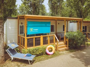A small, single-story cabin with a wooden deck, a lounge chair, and a visible 'roan' sign. - Premium Coastal Lodge Escape for 6 (Brtonigla)