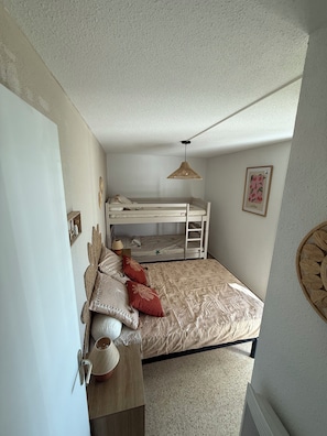 A bedroom with a bunk bed, a bedside table with a lamp, and a wall decoration. - Cosy T2 200m from the beach + private parking (Le Grau-du-Roi)