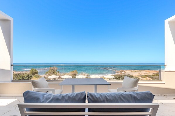 A balcony with a table and two chairs, overlooking a beach and ocean. - Elmar bay Villa (Hersonissos)
