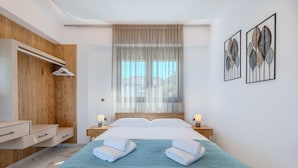 A modern bedroom with a bed, bedside tables, a wooden wardrobe, and artwork on the wall. - Elmar bay Villa (Hersonissos)