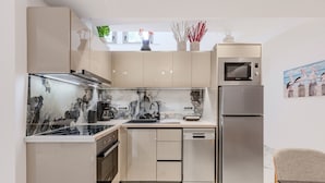 A modern kitchen with a built-in oven, microwave, and dishwasher, marble countertops, and a dining area with a table and chair. - Elmar bay Villa (Hersonissos)