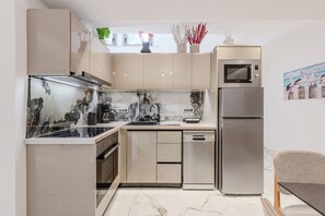 A modern kitchen with a built-in oven, microwave, and dishwasher, marble countertops, and a dining area with a table and chair. - Elmar bay Villa (Hersonissos)