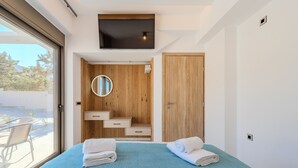 Un dormitorio moderno con cama, televisor, armario de madera y baño con espejo y lavamanos.
