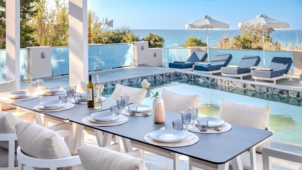 Comedor con vista a la piscina, muebles blancos y una mesa preparada para seis.