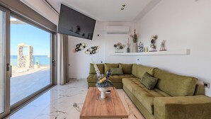 Una sala moderna con un sofá verde, una mesa de centro de madera con un centro de mesa floral, y un ventanal con vistas al mar.