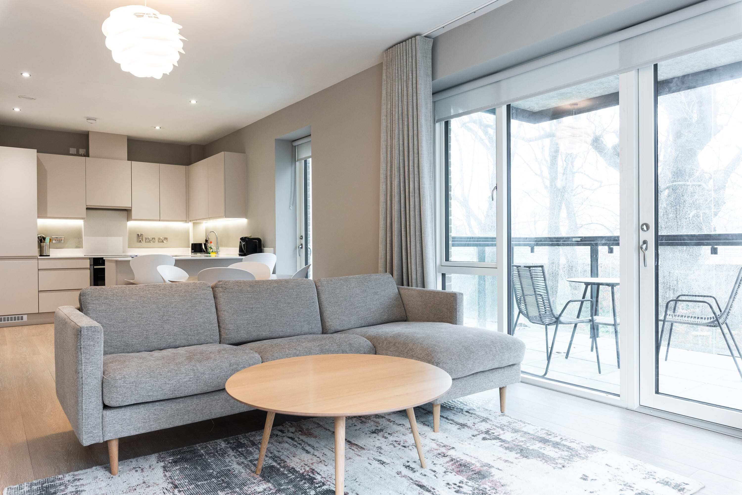 A modern living room with a grey sofa, a round wooden coffee table, and a large sliding glass door leading to an outdoor area.