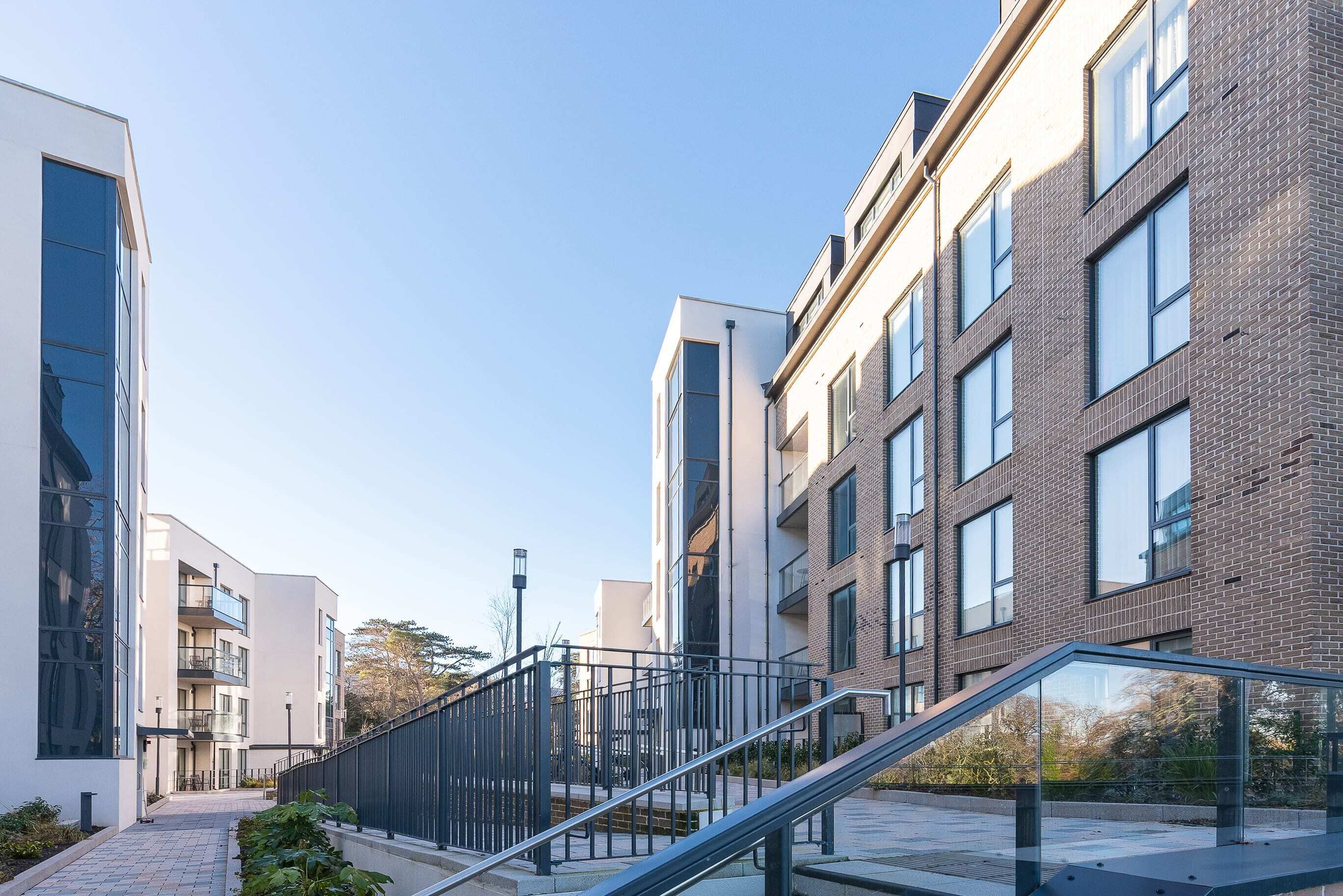 Un edificio moderno con una escalera de cristal, cielo despejado y un sendero pavimentado.