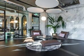 En lobby med en marmorvæg, et rundt bord med stole og en stor stueplante.