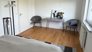 Een slaapkamer met een bed, een bureau, twee stoelen, een hanglamp en een raam.