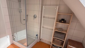 Een douche met een glazen deur, een witte handdoekhouder en een klein plankje met dozen.