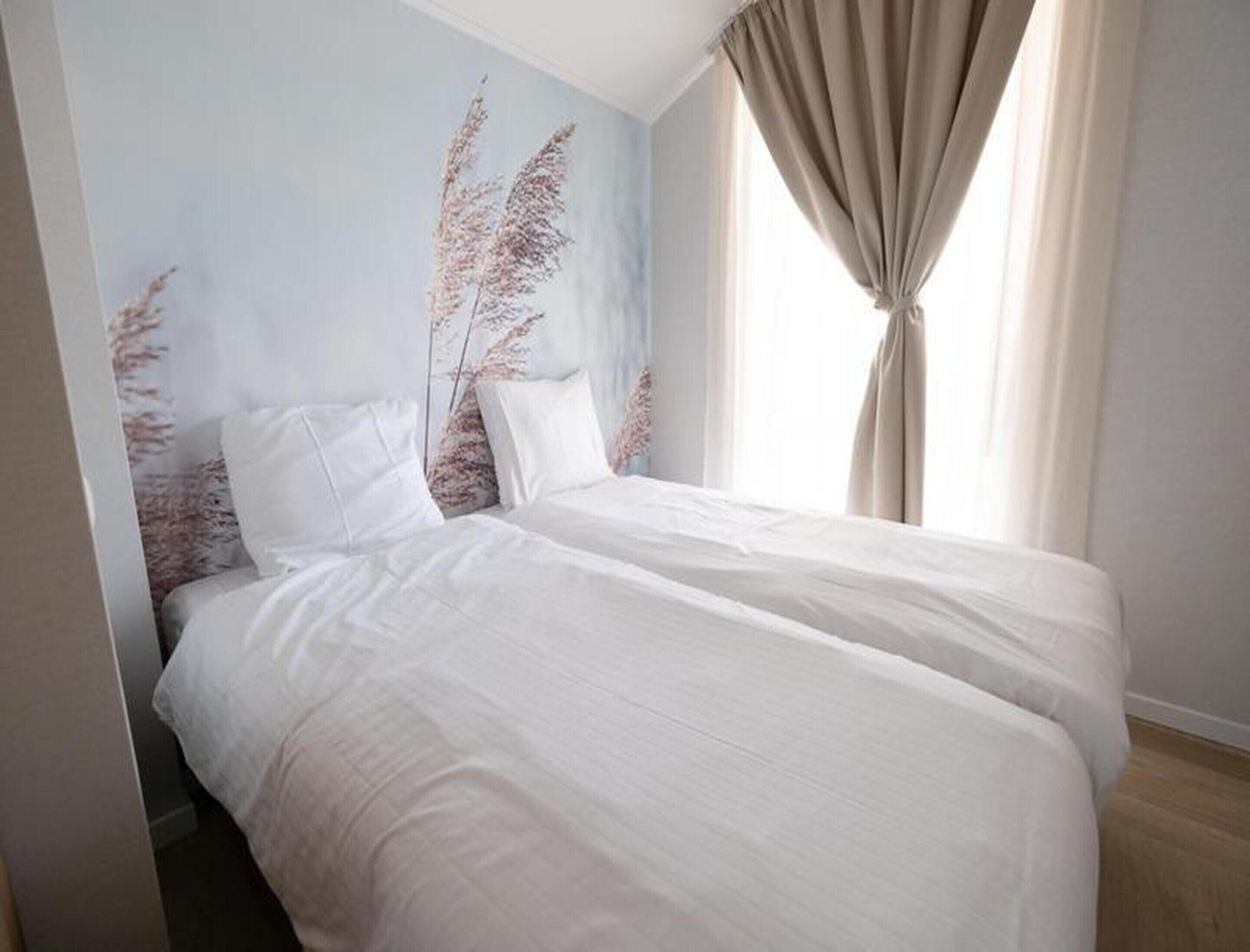 A bedroom with two beds, a large window with curtains, and a wall with a floral mural.