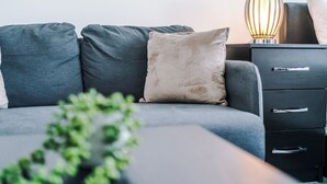 A modern living room with a grey sofa, a beige pillow, a black nightstand with drawers, and a lamp. - Central Nottingham 3 Bed House with Driveway (Nottingham)