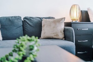 A modern living room with a grey sofa, a beige pillow, a black nightstand with drawers, and a lamp. - Central Nottingham 3 Bed House with Driveway (Nottingham)