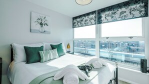 Una camera d'albergo con un letto grande, vista sulla città, una finestra panoramica e un quadro appeso al muro.