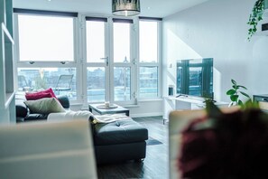 Een moderne woonkamer met een bank, een salontafel, een televisie en grote ramen.