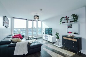 A modern living room with a black sofa, a white coffee table, a black cabinet, and a large window offering a city view. - Skyline 2BD/2BA Central Nottingham Free Parking (Nottingham)