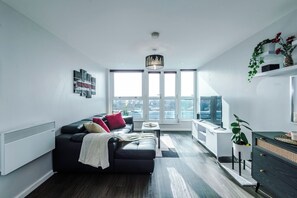 A modern living room with a black sofa, a small coffee table, and a view of the city through large windows. - Skyline 2BD/2BA Central Nottingham Free Parking (Nottingham)