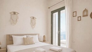 A bedroom with a bed, bedside tables, a window with curtains, and wall decorations. - Elysian Seaside Villa (Almyrida)