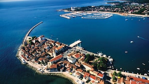 Vista aérea de un pueblo costero con un puerto deportivo destacado, un puerto fortificado y una combinación de edificios residenciales y comerciales.