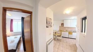 Un pasillo estrecho que conduce a un dormitorio con cama y baño. La habitación tiene un radiador y una ventana con cortinas.