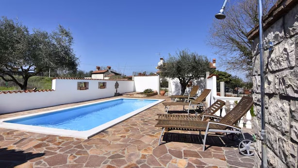 Una piscina con sillas de descanso y un patio de piedra.