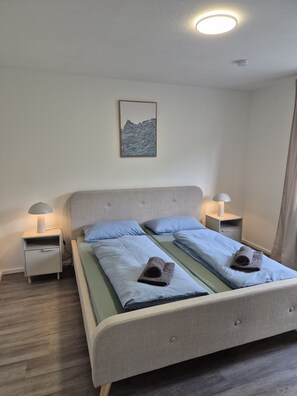 A double bed with two pillows, a bedside table with a lamp, a wall-mounted artwork, and a ceiling light. - Vacation apartment KönigSonne (Lauda-Königshofen)