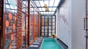 A narrow indoor swimming pool with a tiled floor, glass doors with circular patterns, and a ceiling with a grid structure. - Bumblebee an Artistic Private Villa w/Splash Pool and Pet Friendly (Dehradun)