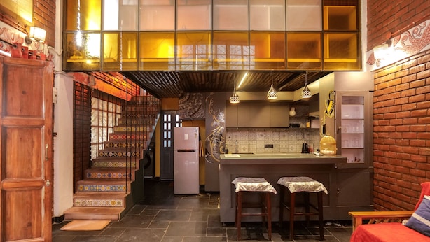 A kitchen with a central island, wooden stools, a refrigerator, and a staircase leading to an upper level. - Bumblebee an Artistic Private Villa w/Splash Pool and Pet Friendly (Dehradun)