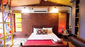 A room with a brick wall, a bed with white bedding, a red blanket, a wooden headboard, a window with yellow blinds, and a wall-mounted air conditioner. - Bumblebee an Artistic Private Villa w/Splash Pool and Pet Friendly (Dehradun)