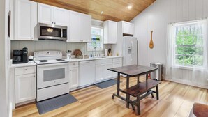 A kitchen with white cabinets, a wooden ceiling, a dining table, and a window with a view of greenery. - The Low Country Loft- Comfy 1BDRM Loft-4 Pass Golf Cart Included (Daufuskie Island)