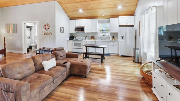 A spacious living room with a wooden ceiling, a sofa, a television, and a kitchen area with white cabinets and appliances. - The Low Country Loft- Comfy 1BDRM Loft-4 Pass Golf Cart Included (Daufuskie Island)