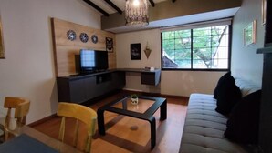 A living room with a sofa, a coffee table, a TV, and a window with a view of greenery. - Libertador Aptos l Jacuzzi l In Provenza (Medellín)