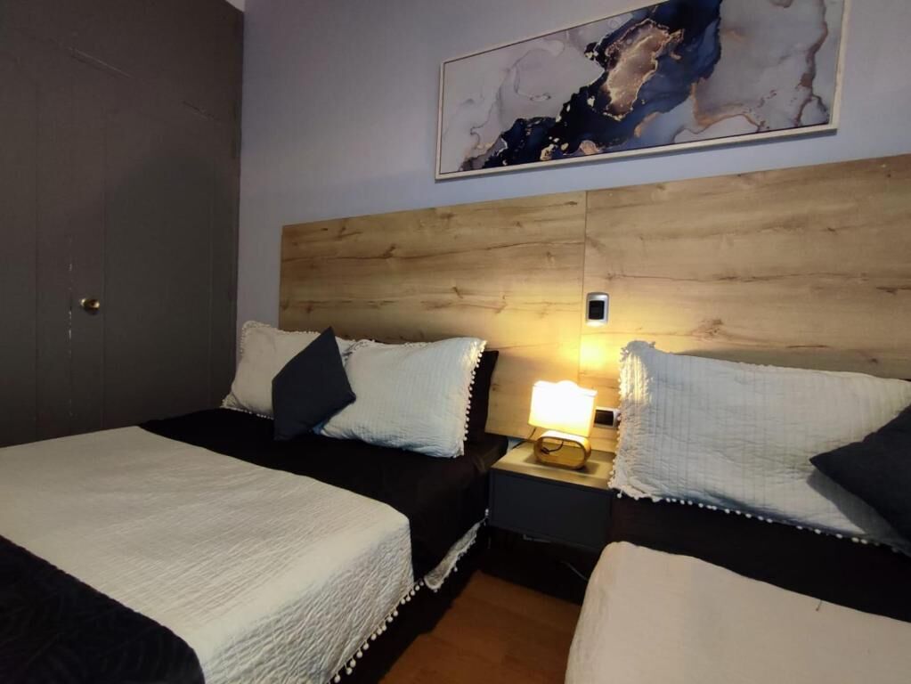 A hotel room with two beds, a wooden headboard, a nightstand with a lamp, and a painting on the wall.