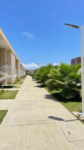 A corridor with a concrete floor, palm trees, and a building with a balcony on the left.